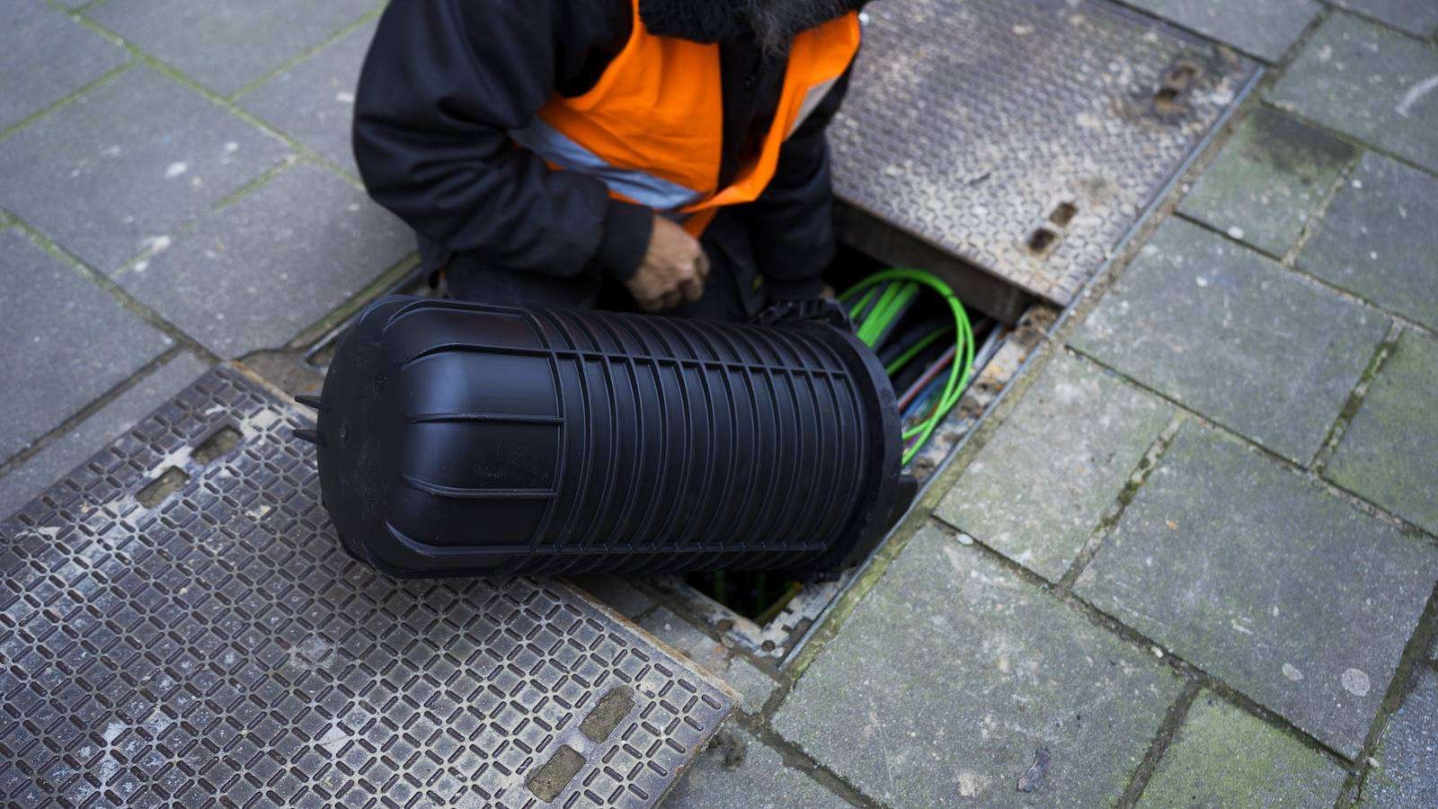 Technicus van A-NET plaatst een glasvezelmof in een straatput