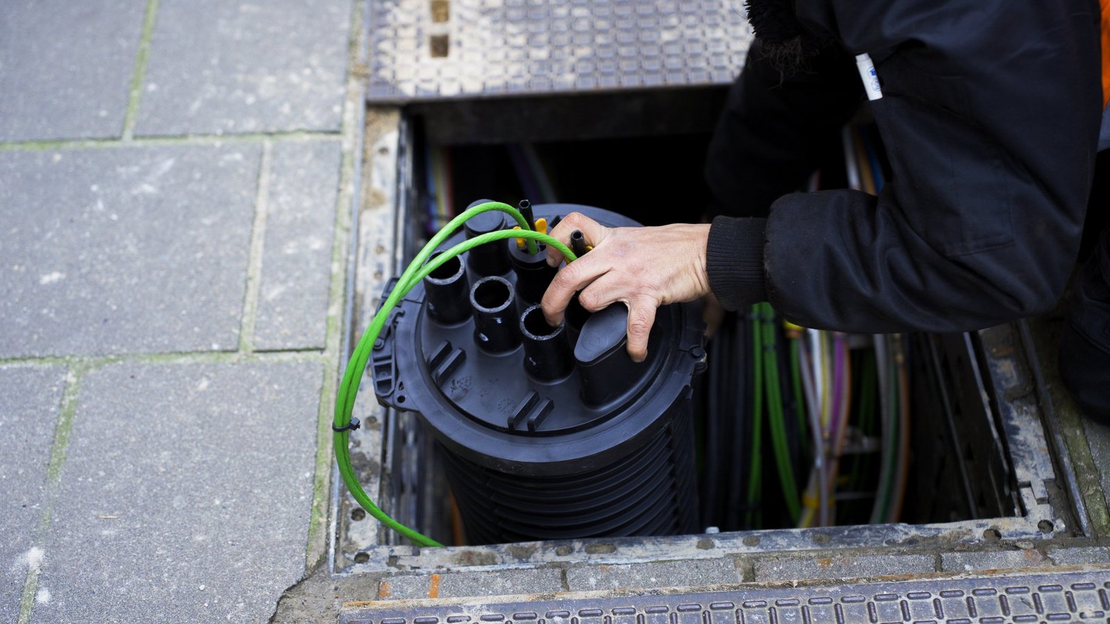 Technicus van A-NET installeert een glasvezelmof in een straatput in Brussel
